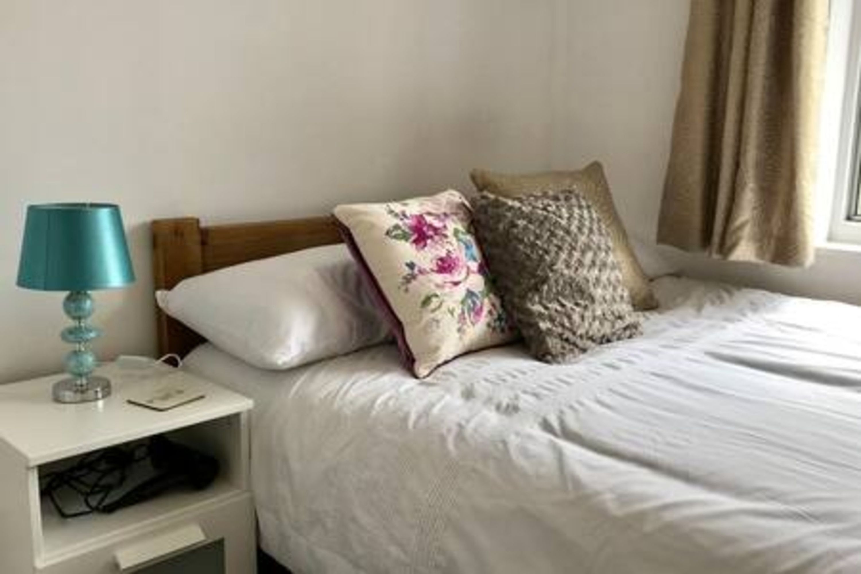 Un lit bien fait, avec une literie blanche et deux coussins décoratifs, une lampe de chevet et une petite commode placée sous le lit.