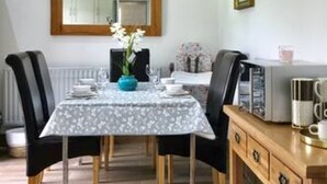 A dining area with a table set for two, a vase of flowers, and a wooden cabinet with a coffee maker. - The Woodfarm Lodge - 3 Bedroom House With Parking (Oxford)