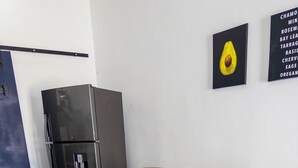 Un coin repas avec une table en verre entourée de chaises, un réfrigérateur et un mur orné d’un tableau encadré.