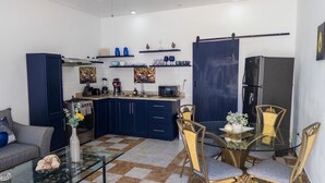 Une cuisine moderne avec des meubles de couleur bleu foncé, un réfrigérateur noir et un coin repas comprenant une table en verre et des chaises dorées.