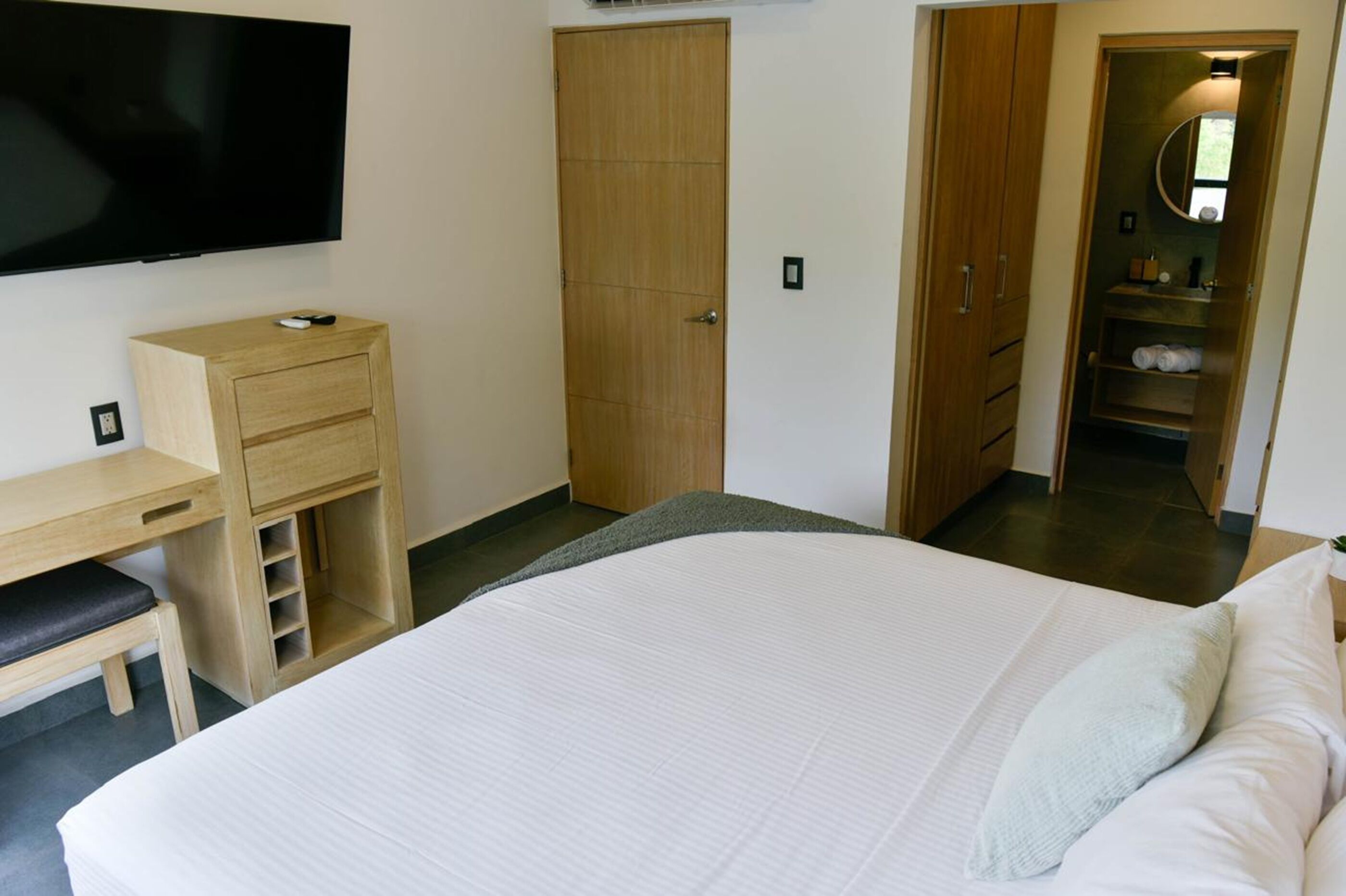 Um quarto com cama, escrivaninha, cadeira, guarda-roupa e televisão.