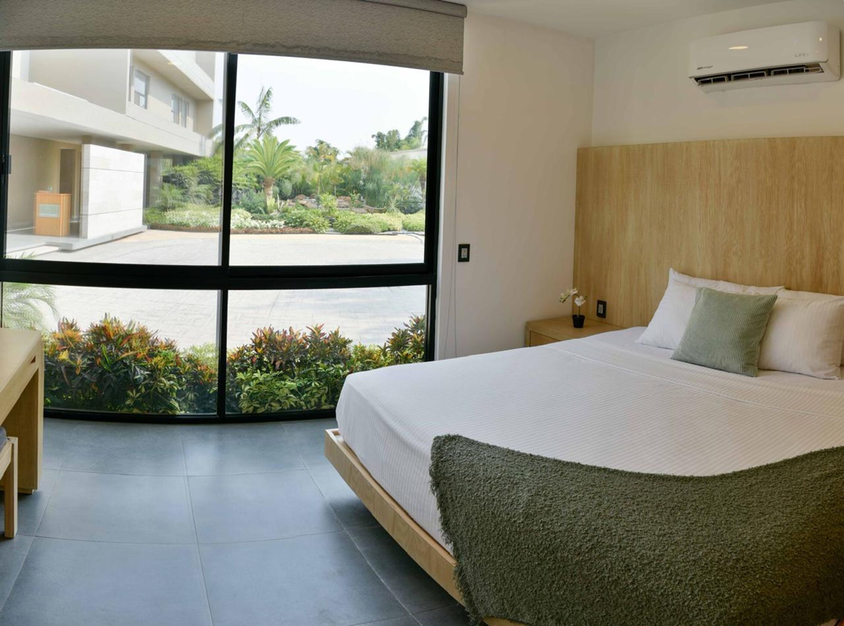 Un dormitorio moderno con una cama grande, cabecera de madera y vistas a un jardín por un ventanal corredero.