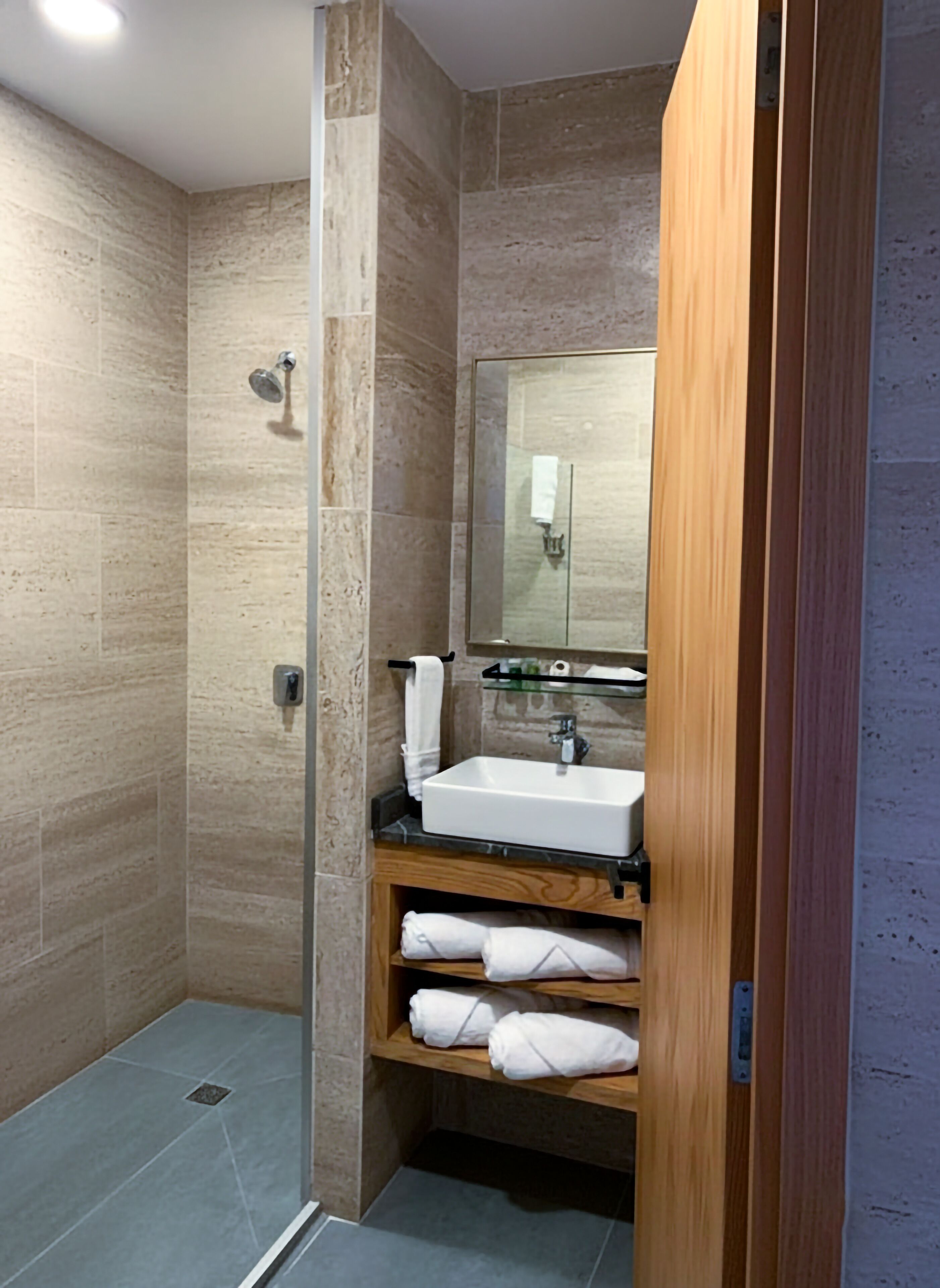 A modern bathroom with a glass-enclosed shower, a white sink, and wooden shelves with towels.