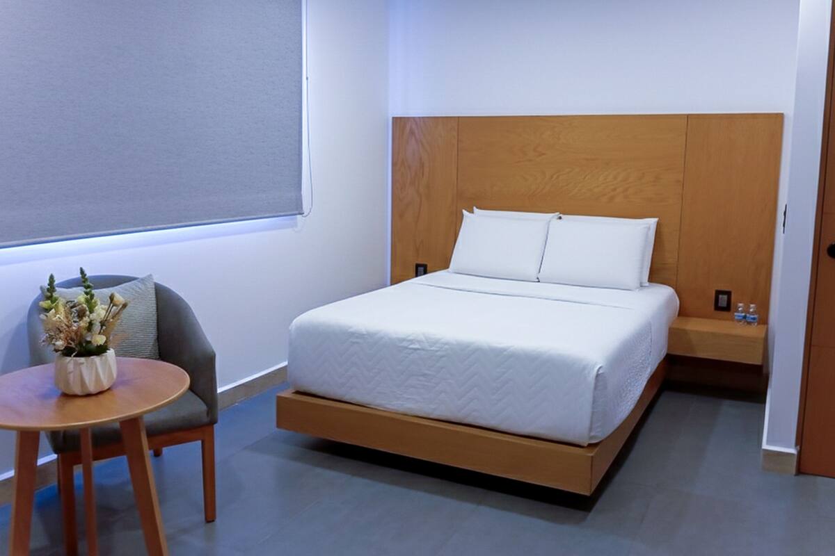 Habitació d'hotel moderna amb un llit, una taula petita amb un ram de flors, una cadira i una porta de fusta.