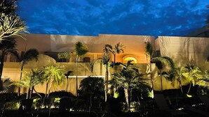 Une cour d’hôtel au crépuscule, avec des palmiers et des chaises longues.