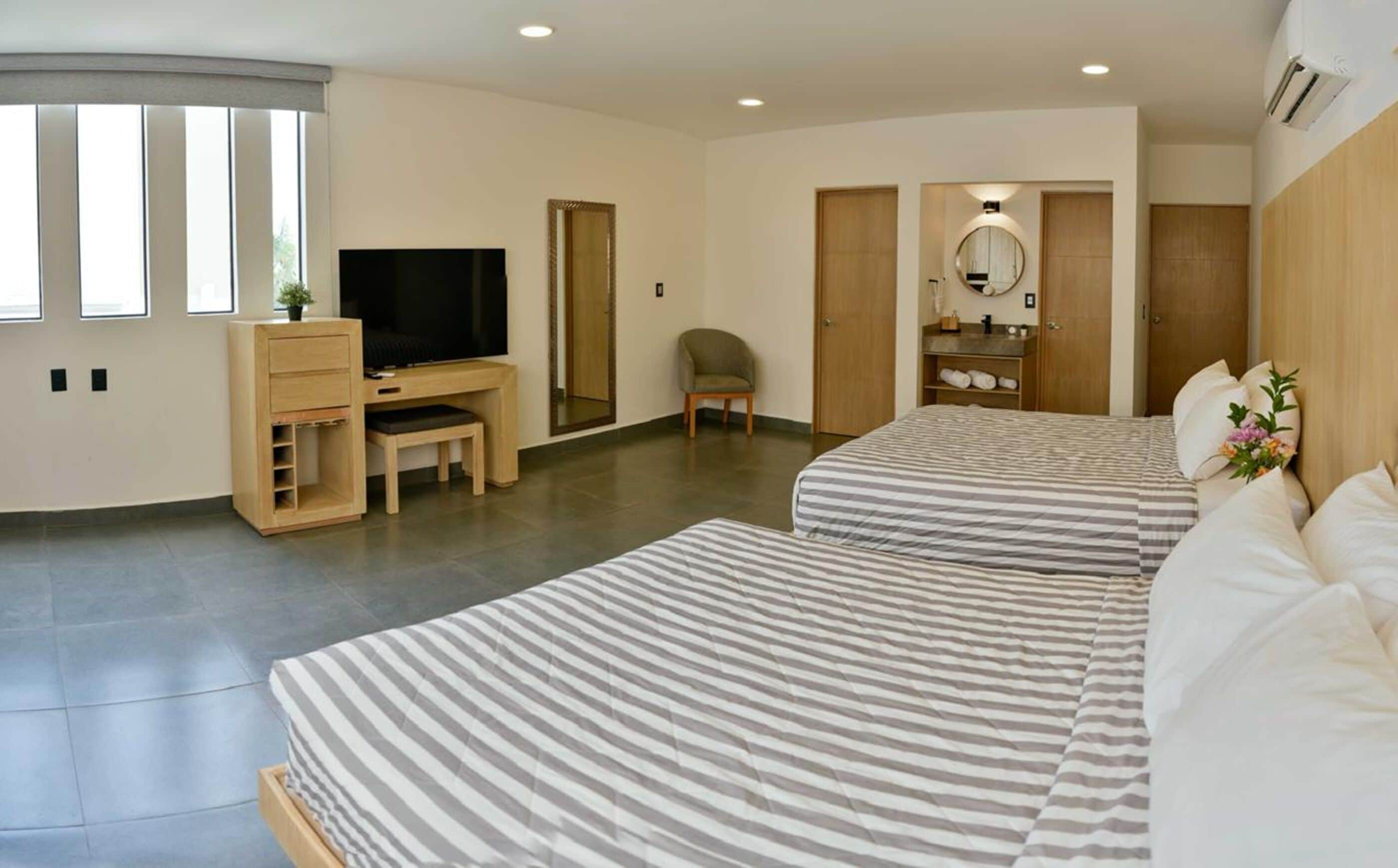 A modern hotel room with a large bed, a desk with a TV, a chair, and a wardrobe.