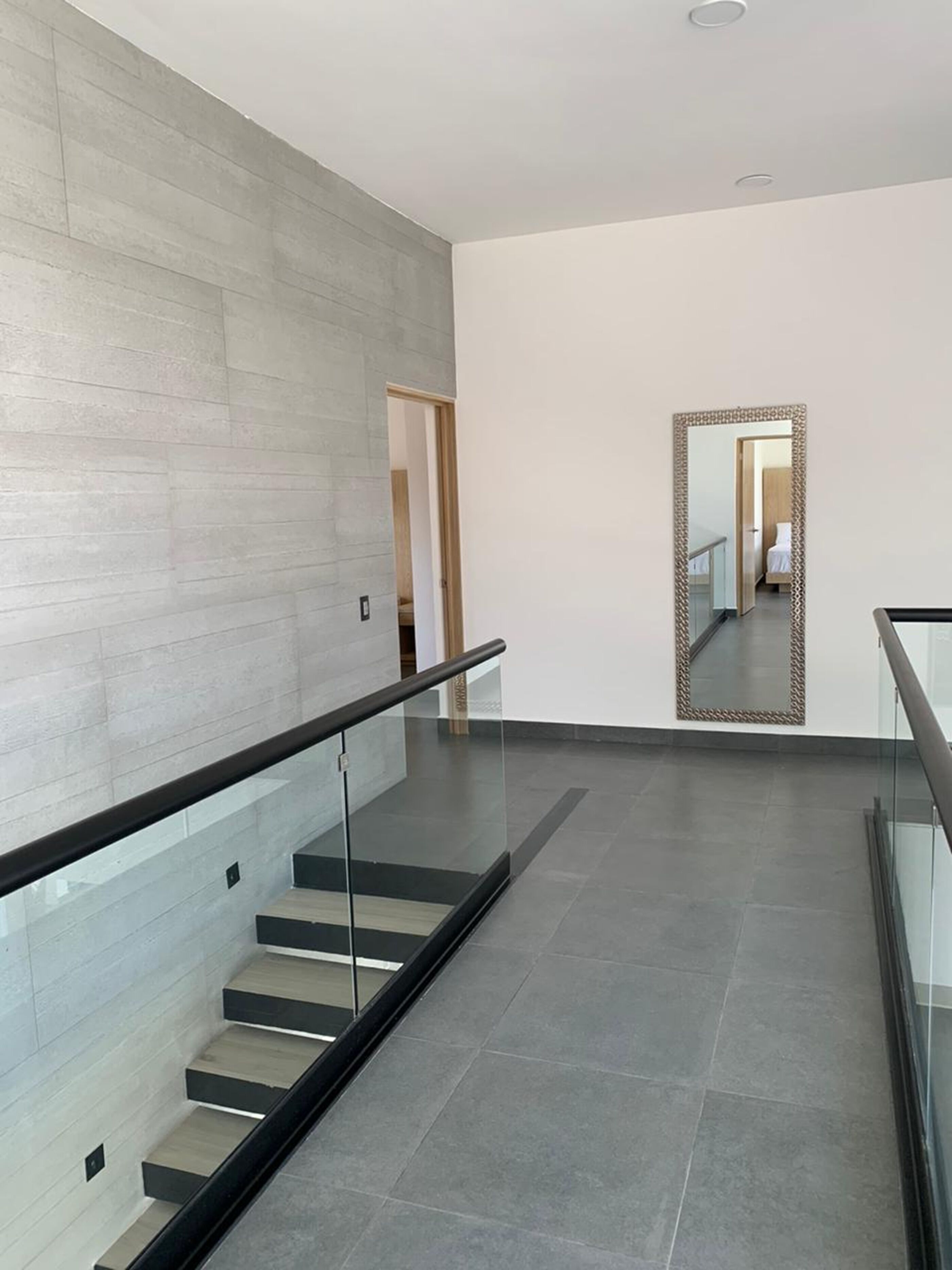 Un interior moderno con una escalera, un espejo y un pasillo que conduce a un dormitorio.