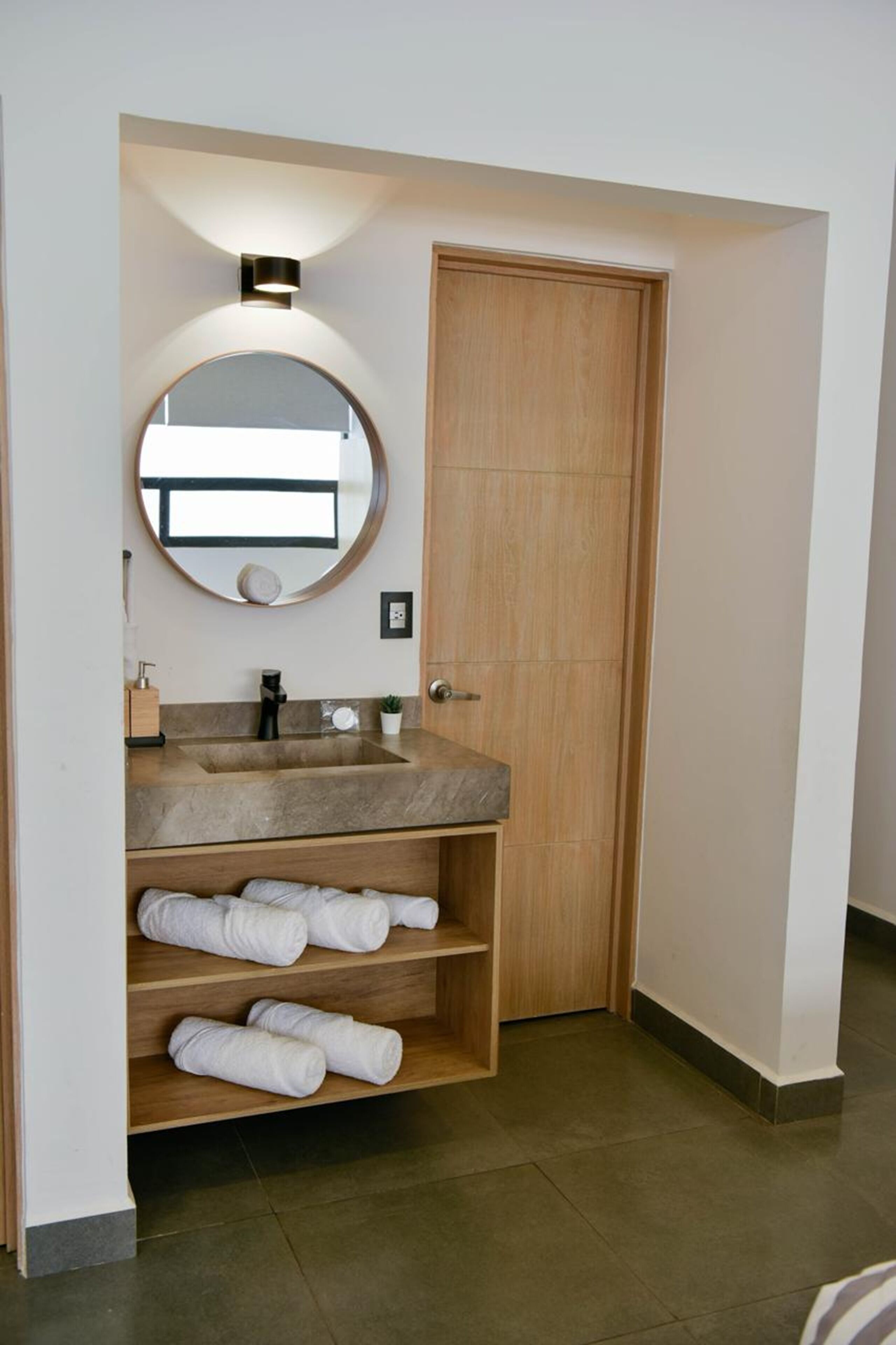 Un baño con tocador de madera, un espejo redondo, un lavabo y un estante para toallas.