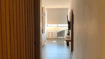 Un pasillo con una puerta de madera, una mesita, una silla y una ventana con persianas.