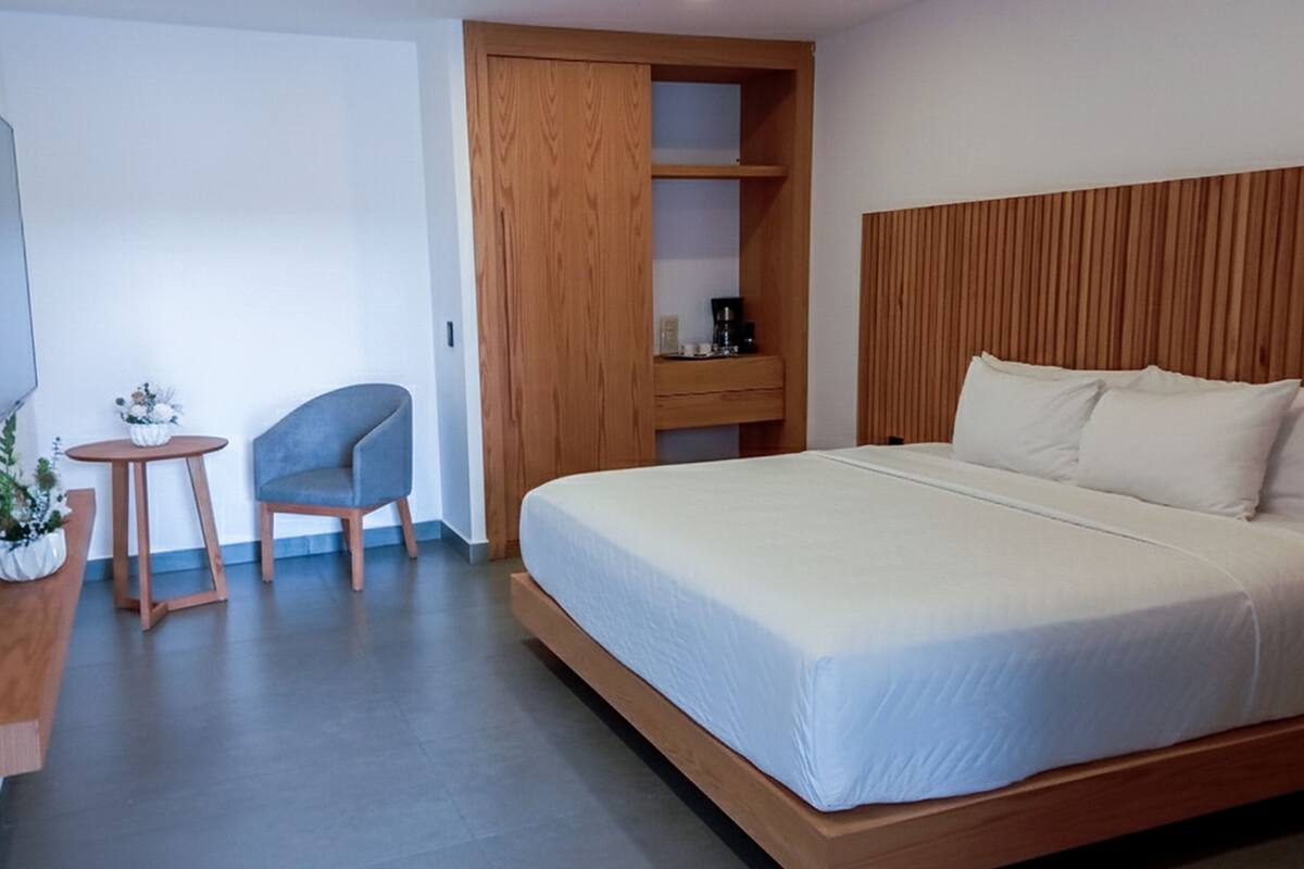 Habitació d'hotel amb llit, televisió, cadira, taula petita i armari de fusta.