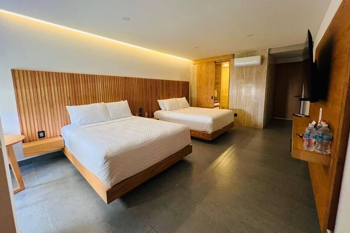Habitació d'hotel moderna amb dos llits, un capçal de llit de fusta, prestatges integrats i una televisió de pantalla plana.