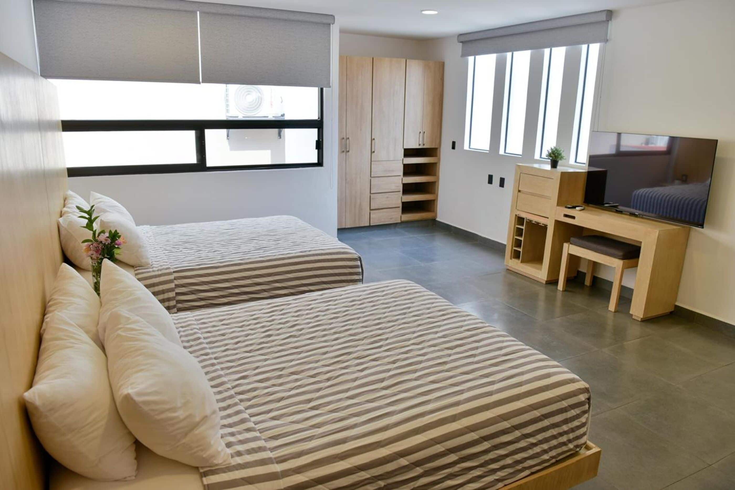 Un dormitorio moderno con dos camas, un escritorio, un televisor y un armario.