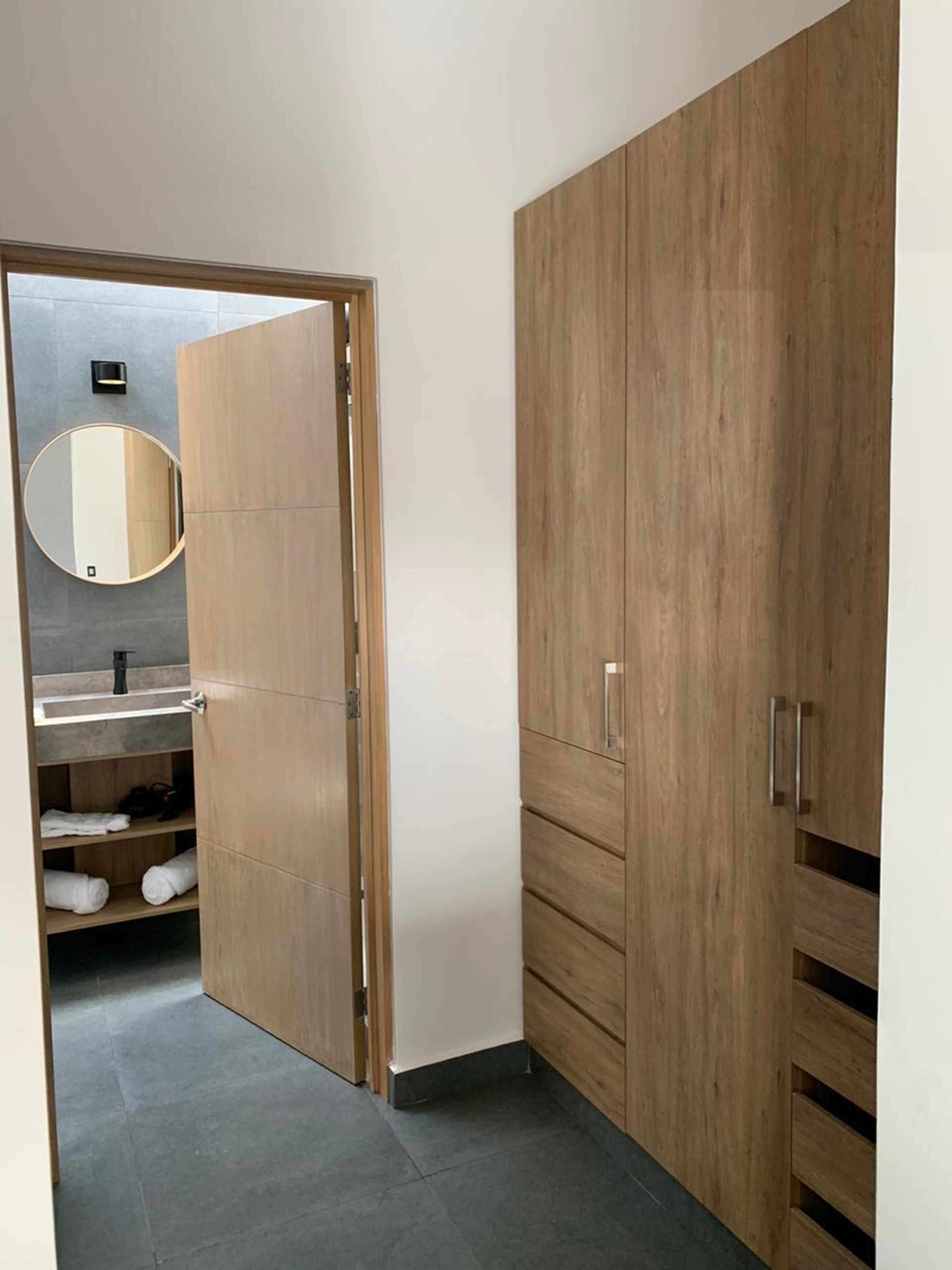 Un baño moderno con tocador de madera, espejo redondo y estante empotrado con toallas.