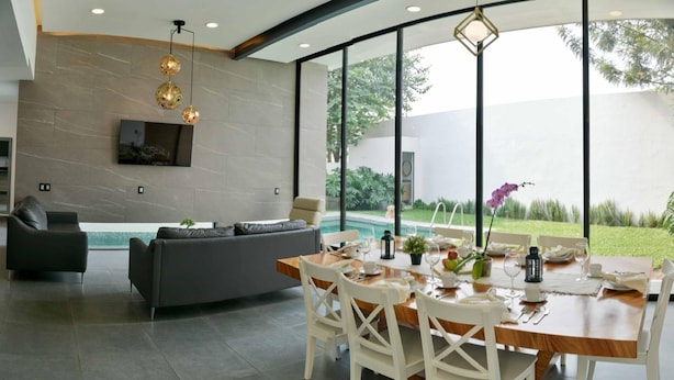 Un espace de repas moderne avec une grande fenêtre, une piscine et un canapé gris.