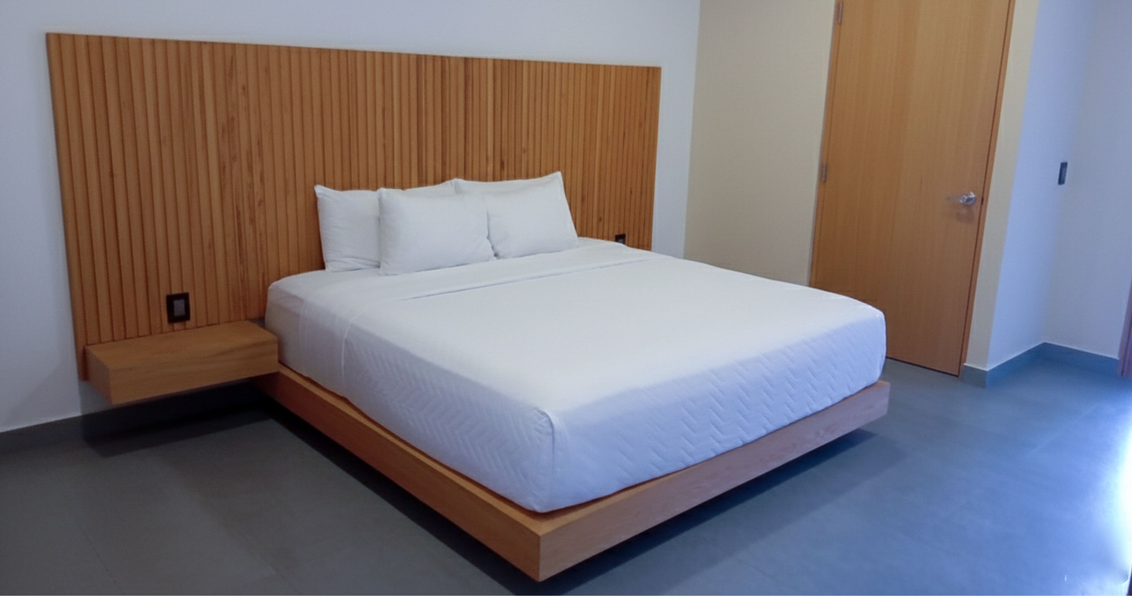 Una cama con cabecera de madera, un banco de madera y una puerta a la derecha.