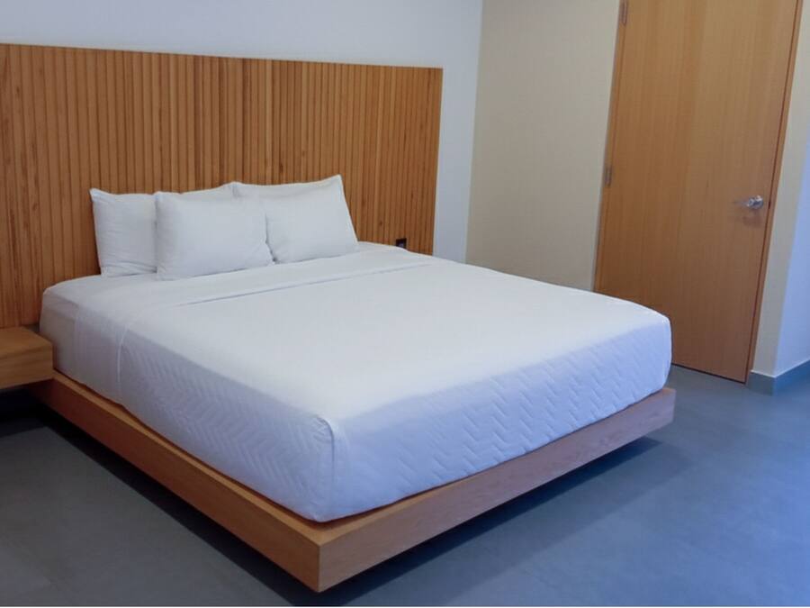 Una cama con cabecera de madera, un banco de madera y una puerta a la derecha.