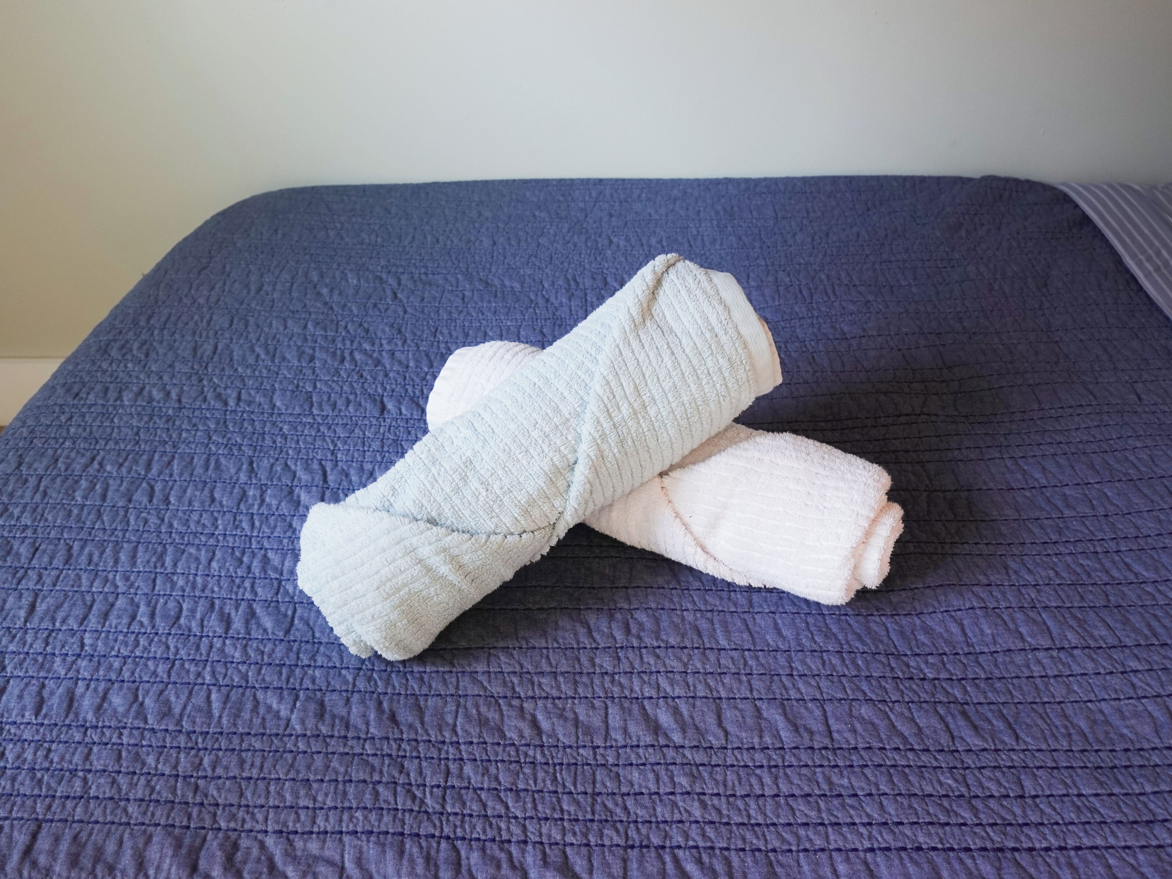 Una cama con un edredón azul y dos toallas blancas enrolladas.