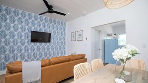 A modern living room with a patterned wall, a brown sofa, a dining table with chairs, and a ceiling fan.
