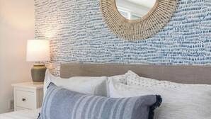 A neatly made bed with a striped pillow and a white pillow with a pattern. There is a bedside table with a lamp and a decorative mirror on the wall.