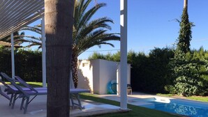 Un área junto a la piscina con sillones de descanso, una zona de estar techada y una piscina pequeña.