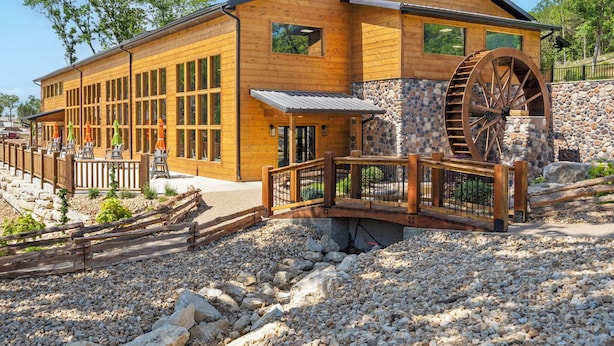 Ein Gebäude aus Holz mit großen Fenstern, einer Steinmauer und einem Wasserrad.