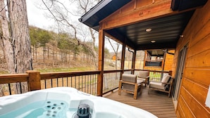 Ein Whirlpool auf einer Holzterrasse, umgeben von Bäumen und mit Gartenmöbeln.