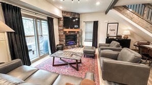 Ein modernes Wohnzimmer mit Kamin aus Stein, Ledersofas, einem Couchtisch und einer Treppe.