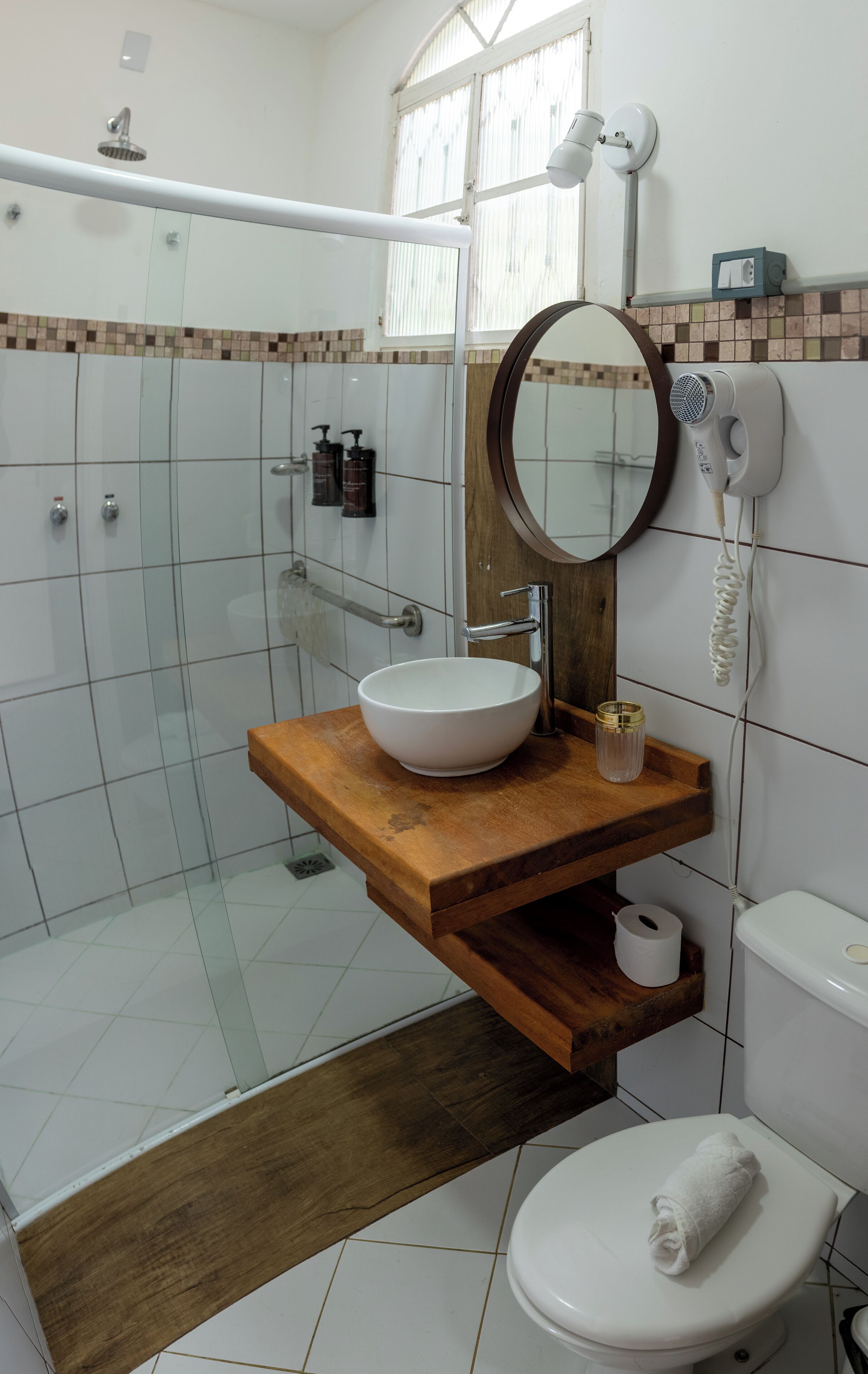 Un bagno con un mobile bagno in legno, un lavandino bianco, uno specchio, un WC e uno spazio doccia.
