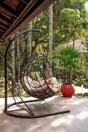 A hanging chair with a floral cushion, a red planter with a tall plant, and a wooden structure. - Pousada Quinta dos Doges Ltda (Valenca)