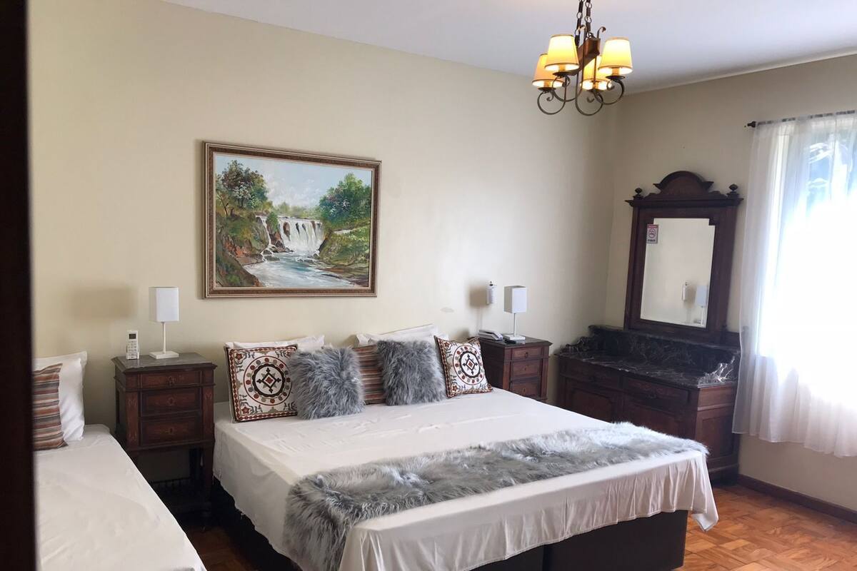 A bedroom with a large bed, a nightstand, a dresser, a mirror, and a painting of a waterfall on the wall.