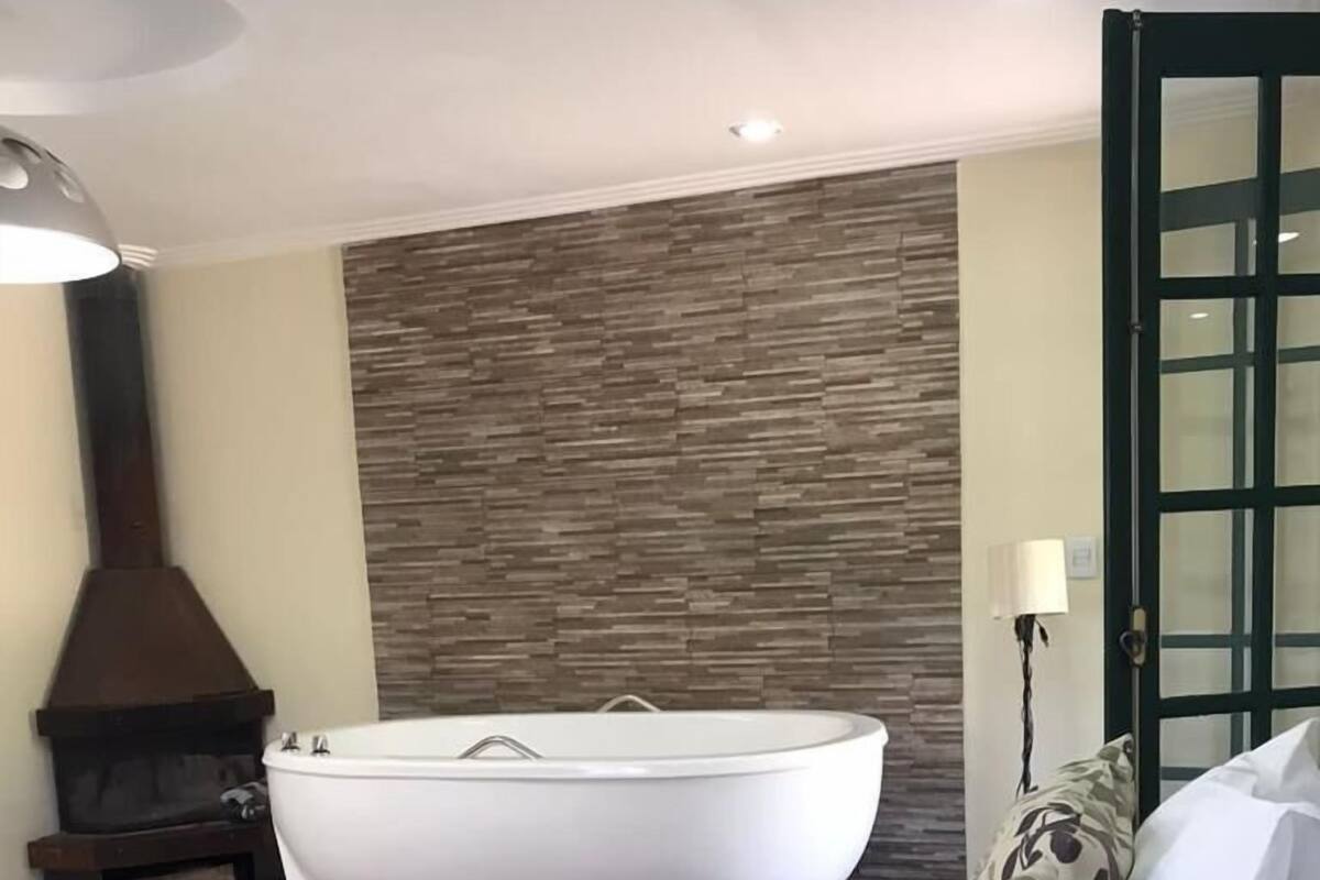 A modern bedroom with a large bathtub, a wooden wall, and a fireplace.