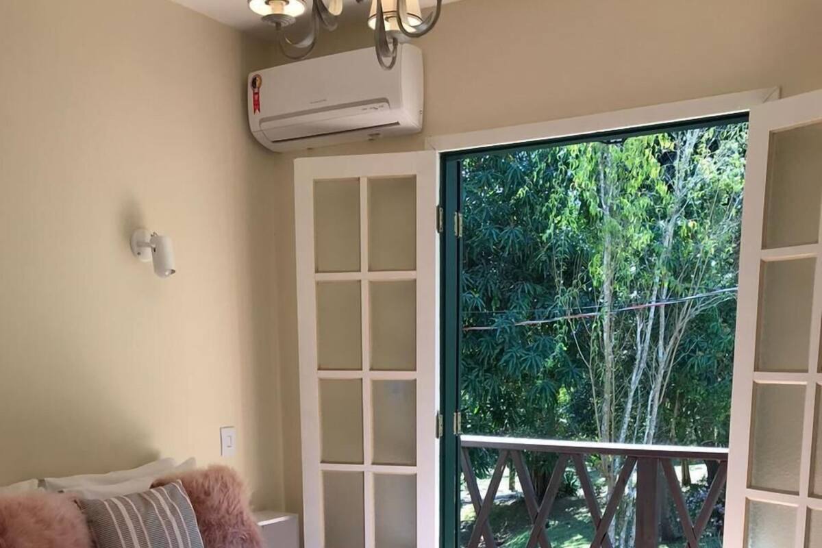 A bedroom with a large bed, a view of greenery through a glass door, and a ceiling fan.