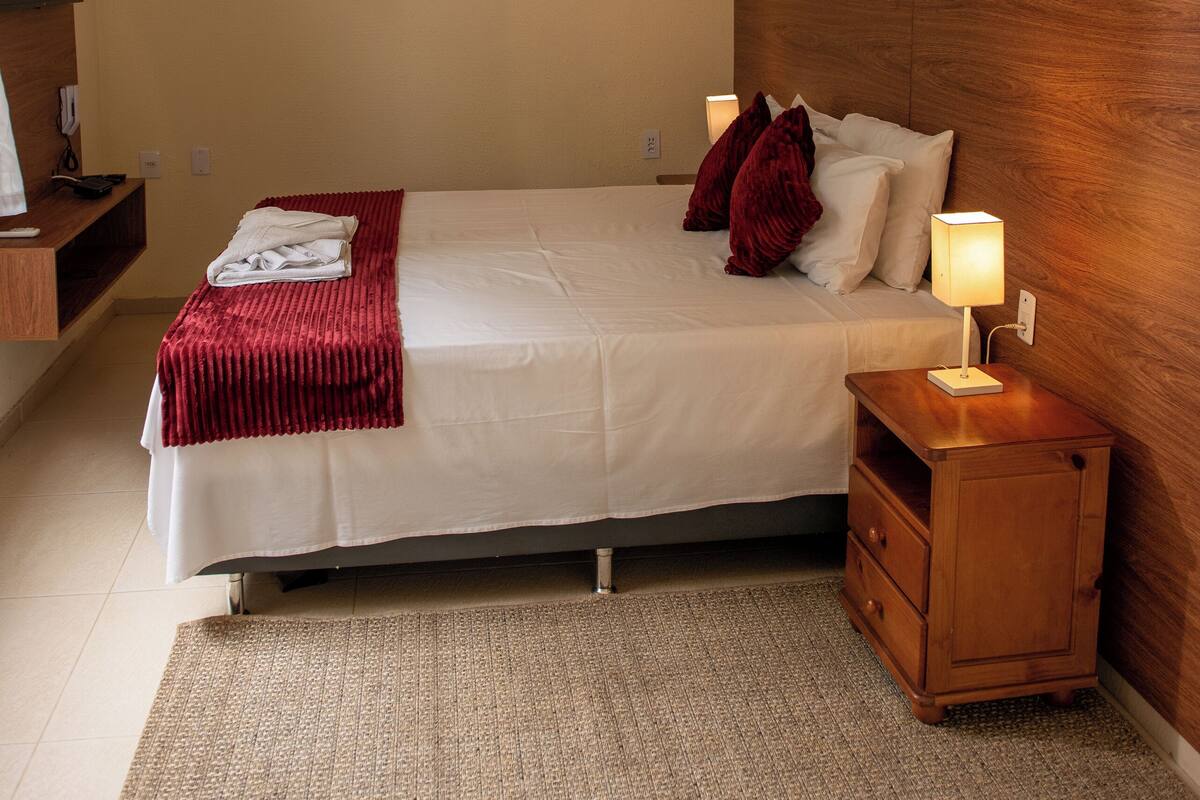 A neatly arranged hotel room with a bed, bedside table, lamp, and wall-mounted air conditioning unit.