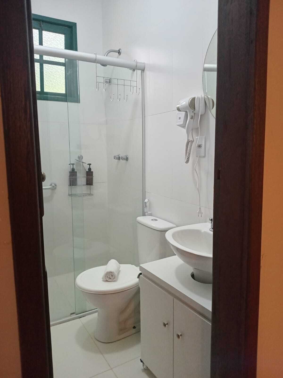 Um banheiro moderno com box de vidro, vaso sanitário, pia e secador de cabelo fixado na parede.