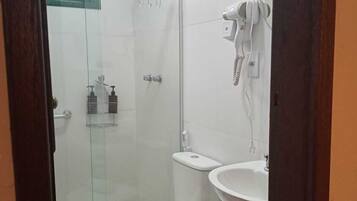 Um banheiro moderno com box de vidro, vaso sanitário, pia e secador de cabelo fixado na parede.