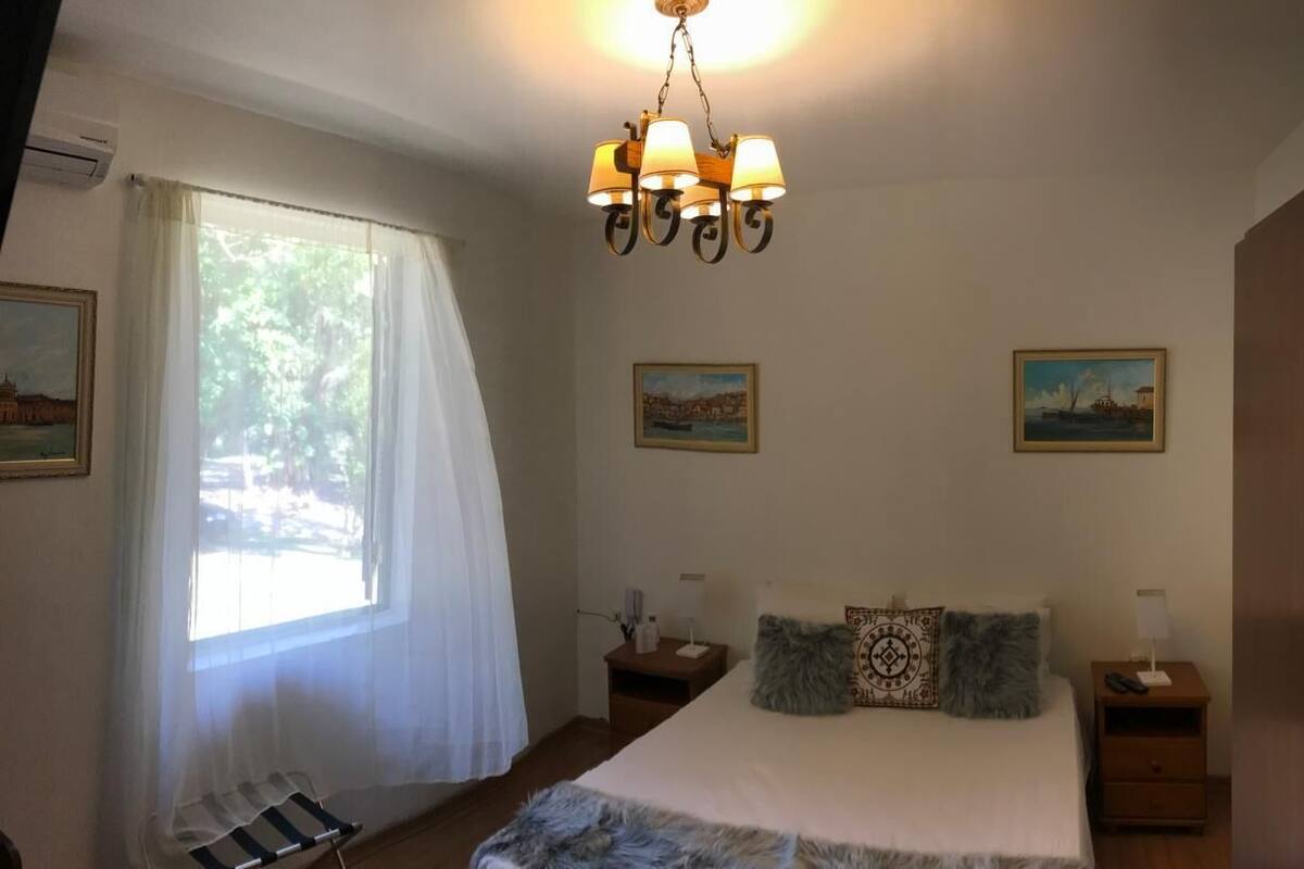 A bedroom with a bed, two bedside tables, a hanging lamp, a chair, and two paintings on the wall.