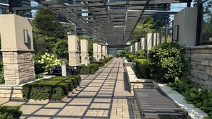A covered pedestrian walkway with stone pillars, benches, and greenery.