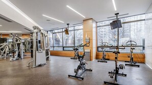 A gym with stationary bikes, weight machines, and a large window with a city view.
