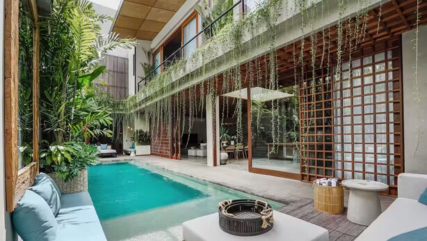 A pool area with a seating arrangement, surrounded by lush greenery and traditional wooden structures. - Designers Dream Near Beach (Bali)