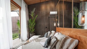 A modern bedroom with a wooden headboard, a large bed with multiple pillows, a potted plant, and a wall-mounted air conditioner. - Designers Dream Near Beach (Bali)