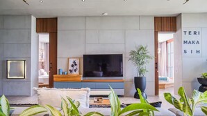 A modern living room with a large flat-screen TV, wooden paneling, and potted plants. - Designers Dream Near Beach (Bali)