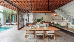 A modern dining area with a wooden table and chairs, a view of a pool, and a staircase leading to a loft area. - Designers Dream Near Beach (Bali)