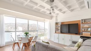 Een moderne woonkamer met een groot raam, een eethoek en een inbouwtelevisieplank.