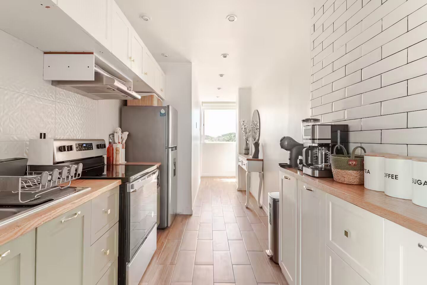 A modern kitchen with stainless steel appliances, white cabinetry, and a wooden countertop.