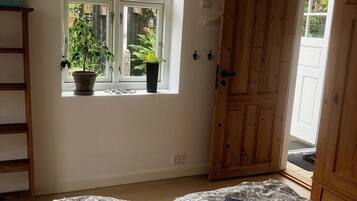 Un dormitorio con dos camas, una ventana con plantas, una puerta de madera y un estante pequeño.