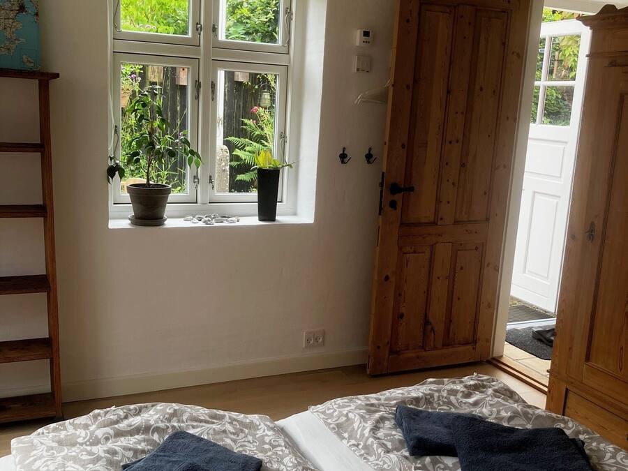 Un dormitorio con dos camas, una ventana con plantas, una puerta de madera y un estante pequeño.
