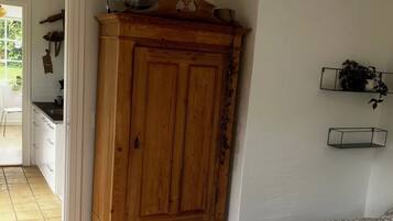 A bedroom with a wooden wardrobe, a bed with patterned bedding, and a small shelf with plants.