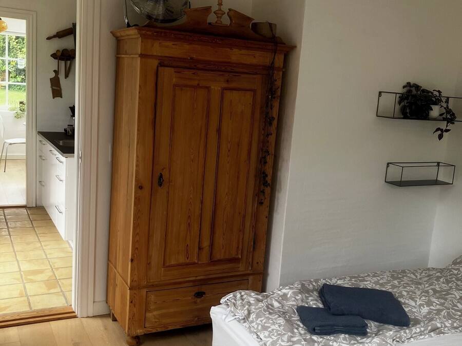 A bedroom with a wooden wardrobe, a bed with patterned bedding, and a small shelf with plants.