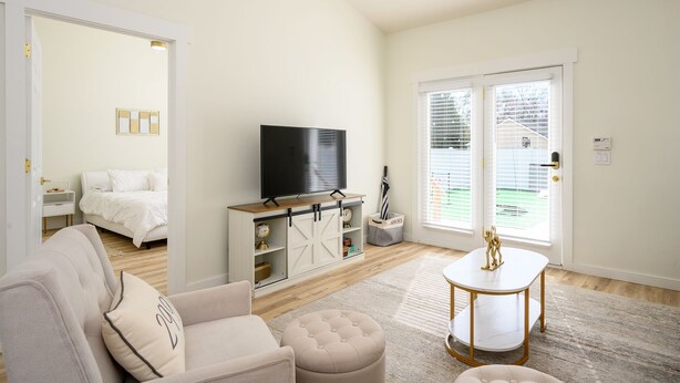 A living room with a sofa, ottoman, TV, and a small table. There is a bed in the background and a door leading outside. - Bluffton Lowcountry Casa Del Café/Private Driveway+Fence Yard (Bluffton)