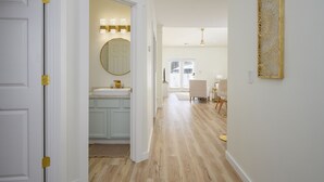 A hallway with a white door, a bathroom with a sink and mirror, and a dining area with chairs and a table. - Bluffton Lowcountry Casa Del Café/Private Driveway+Fence Yard (Bluffton)